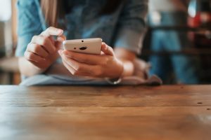 Hand,Of,Woman,Using,Smartphone,On,Wooden,Table,space,For,Text